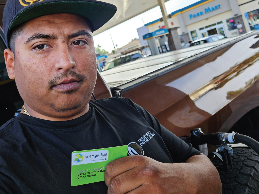 A picture of a person holding an energie·fuel card next to their truck, at one of the gas pumps in the Palomar Valero.