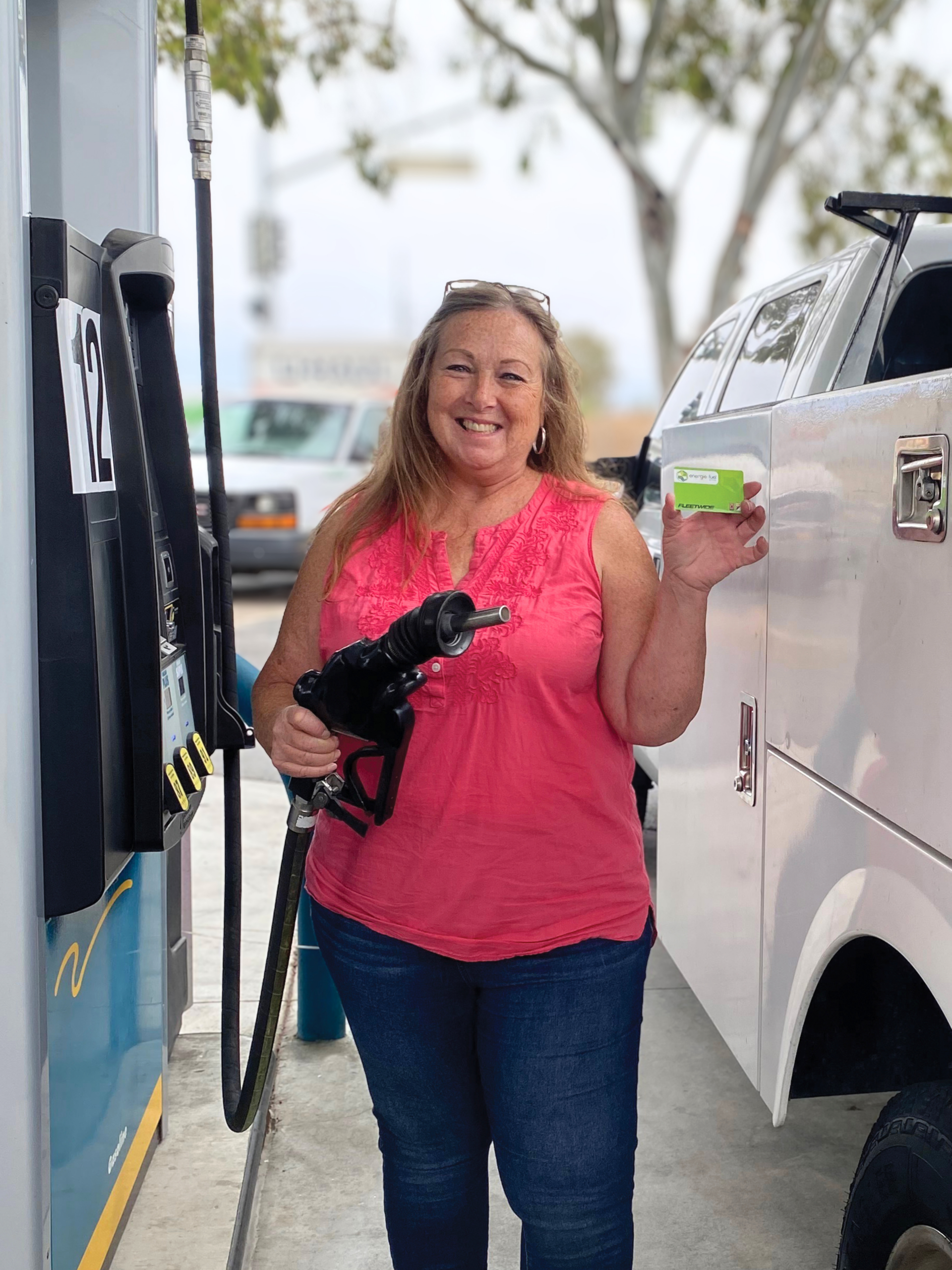 Woman at gas station smiling and holding out Energie Fuel card.